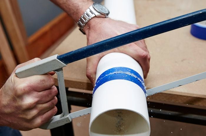 A person sawing through PVC pipe using a hacksaw