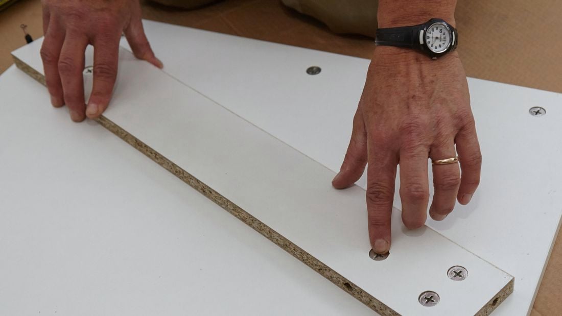 A person attaching a rail to the inside of a cabinet panel