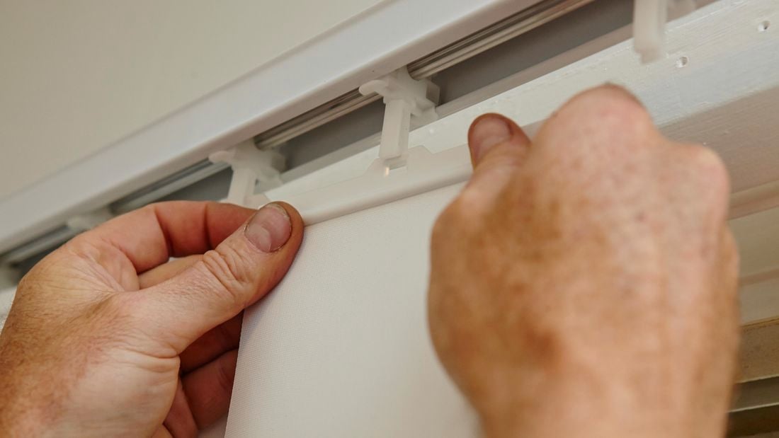 A person hanging a vertical blind on a track