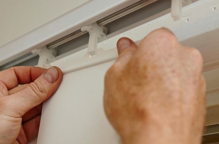 A person hanging a vertical blind on a track