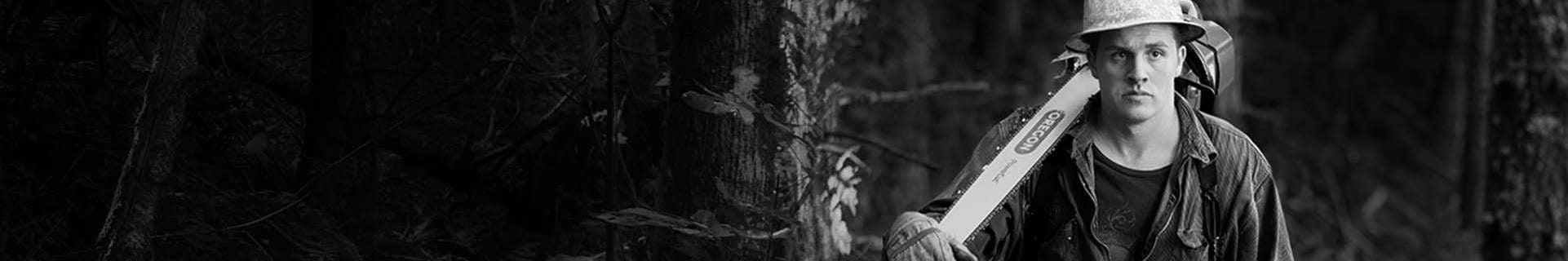 Black and white photo of a male worked wearing protective equipment, carrying a chainsaw over his shoulder