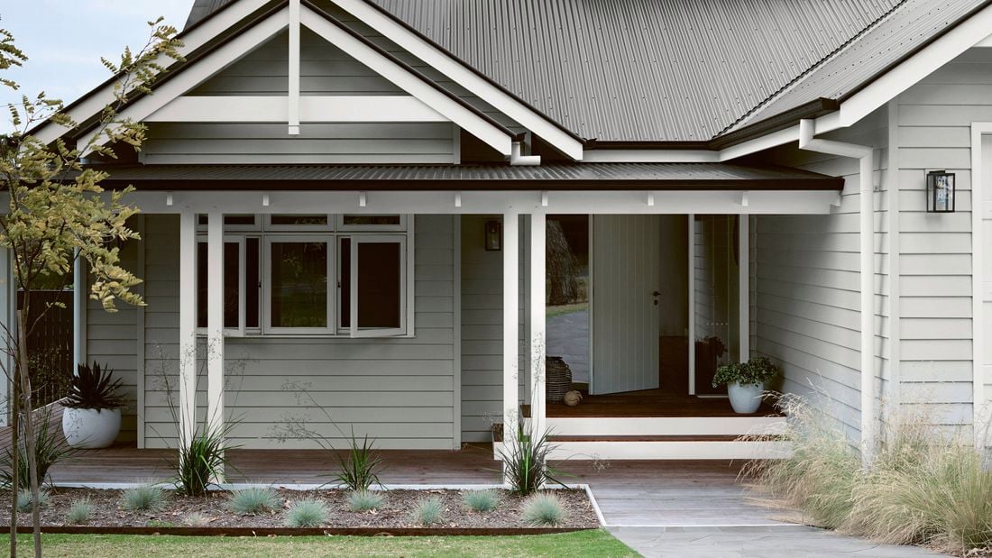 Grey house with white trim and dark corrugated iron roof, front porch with wooden deck, and garden.