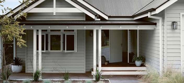 Grey house with white trim and dark corrugated iron roof, front porch with wooden deck, and garden.