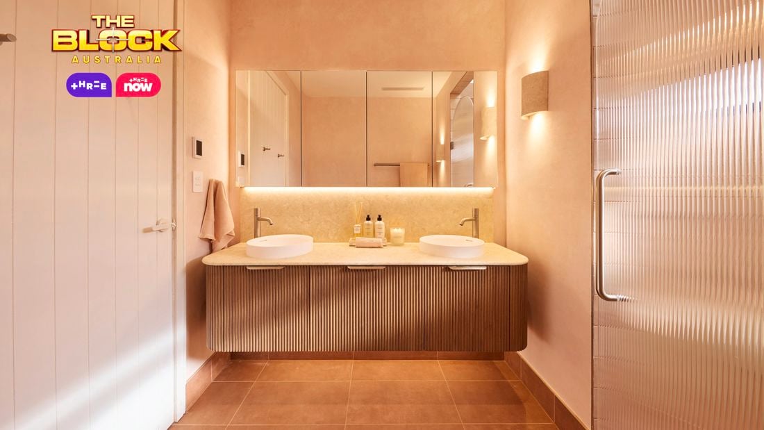 Modern bathroom with double round sinks, chrome faucets, mirrored cabinets, soft pink walls, and toiletries on the vanity. 
