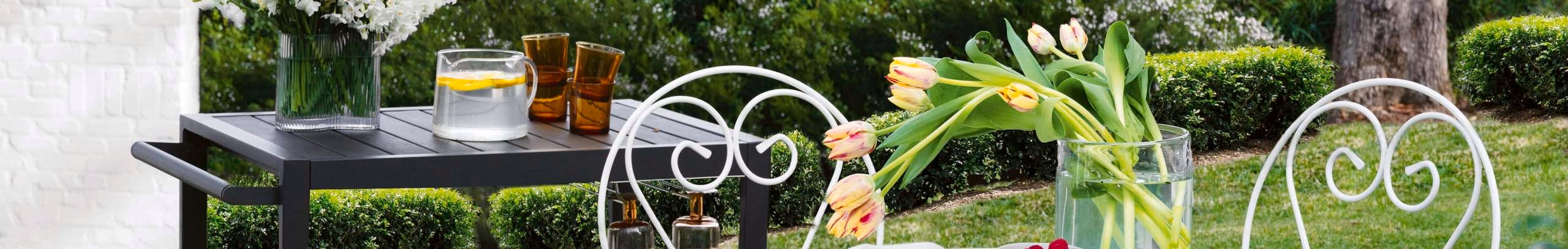 black bar table and white metal outdoor setting on lawn with fresh flowers and fruit