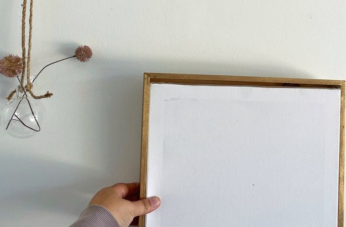 Close up image of a left hand holding a picture frame next to a hanging vase to make a gallery wall