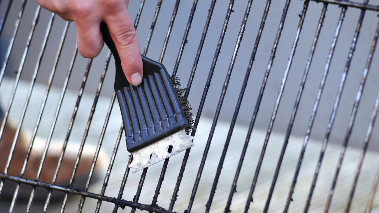 Close up of a hand cleaning a barbeque grill with a cleaning brush