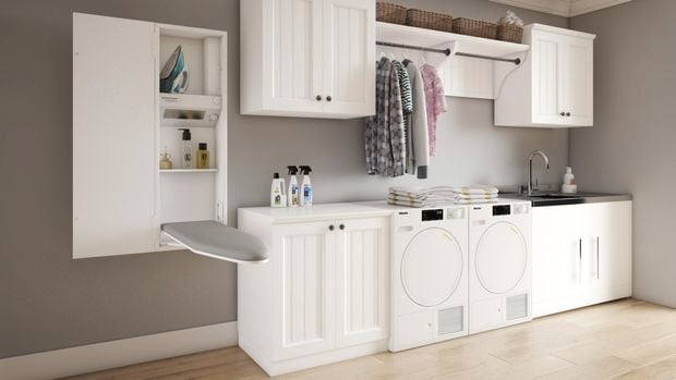 Modern white laundry with a wall mounted ironing board, supertub, washing machines, hanging clothes and storage