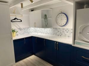 Kitchen with blue cupboards, a white stone benchtop and a clock on the wall.