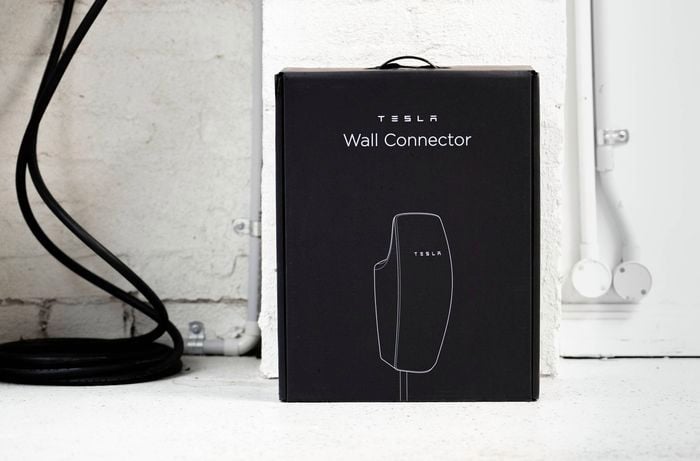 The image shows a boxed Tesla Wall Connector placed on the floor, ready for EV charger installation.   