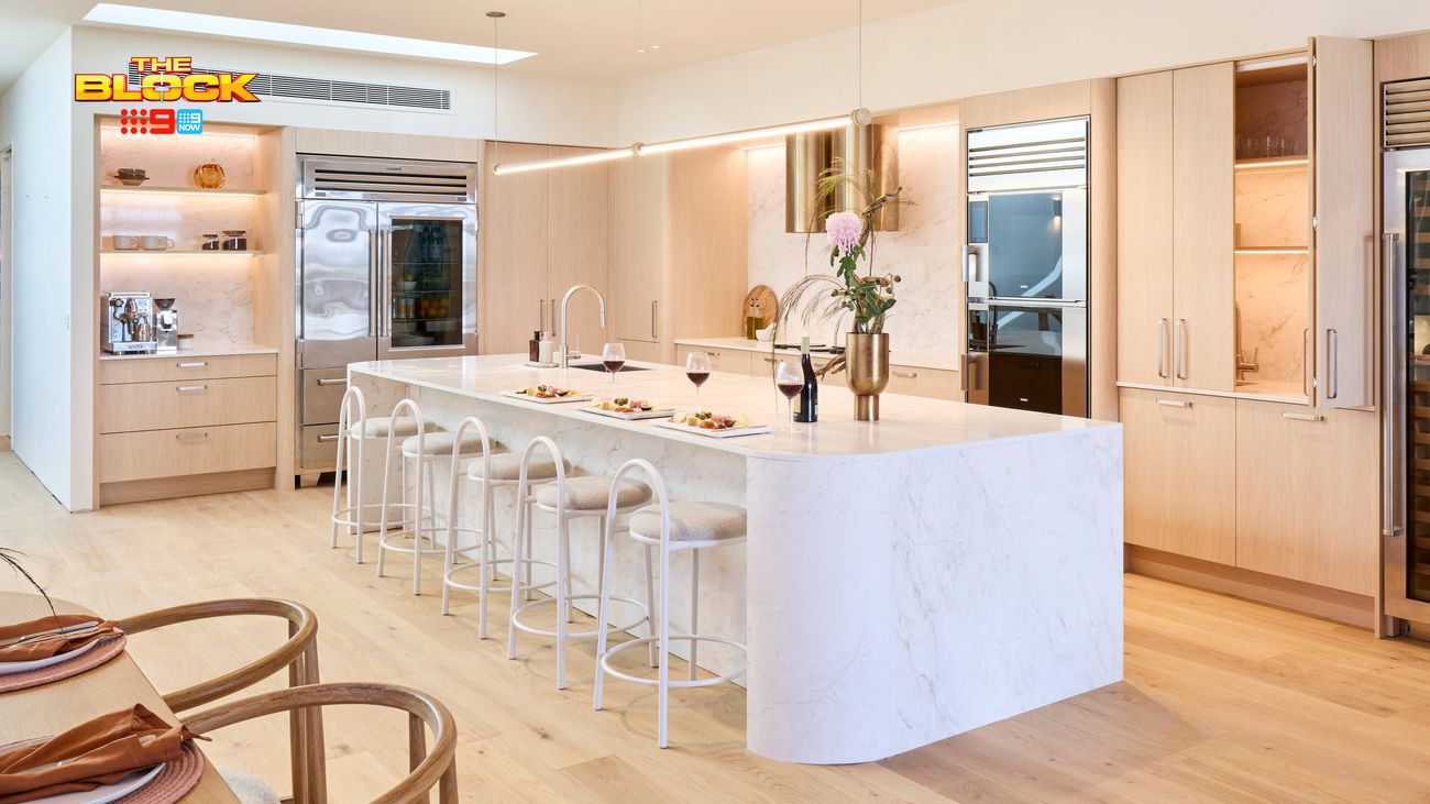 Modern kitchen featuring a curved stone island bench with bar stools, light timber cabinetry and integrated appliances.