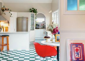 A vibrant kitchen with a green-and-white checkered floor, white cabinetry, a red dining chair and colourful stained-glass windows.