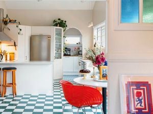 A vibrant kitchen with a green-and-white checkered floor, white cabinetry, a red dining chair and colourful stained-glass windows.