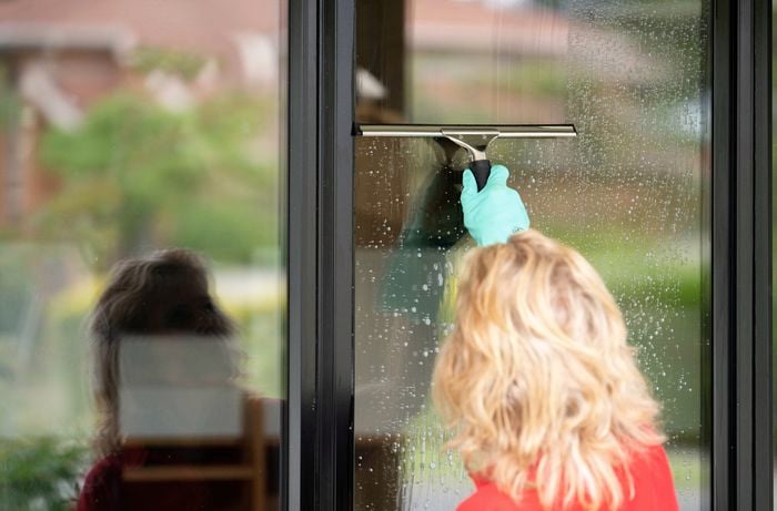 A woman wearing gloves using a squeegee to remove the cleaning solution from a window to achieve a streak-free finish. 