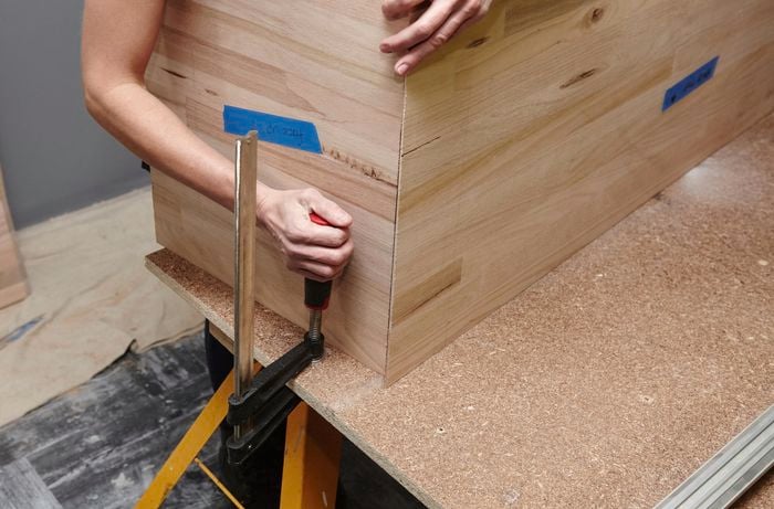 A person placing a clamp next to an L-shaped timber panel