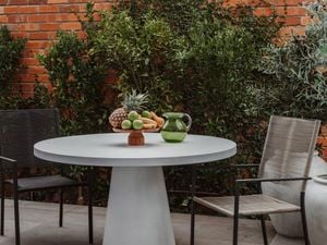 Outdoor furniture set outside, in front of plants and a brick wall