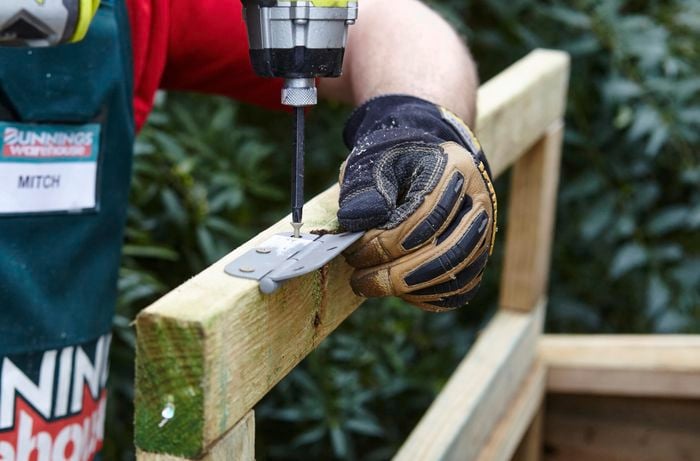 A hinge being screwed into place on a wooden frame as part of a chicken coop hatch