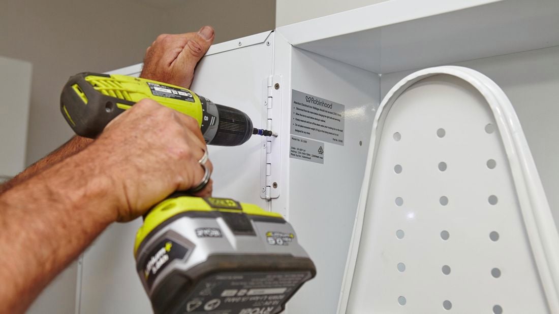 A Bunnings team member using the drill and screws to attach the door to the ironing centre.