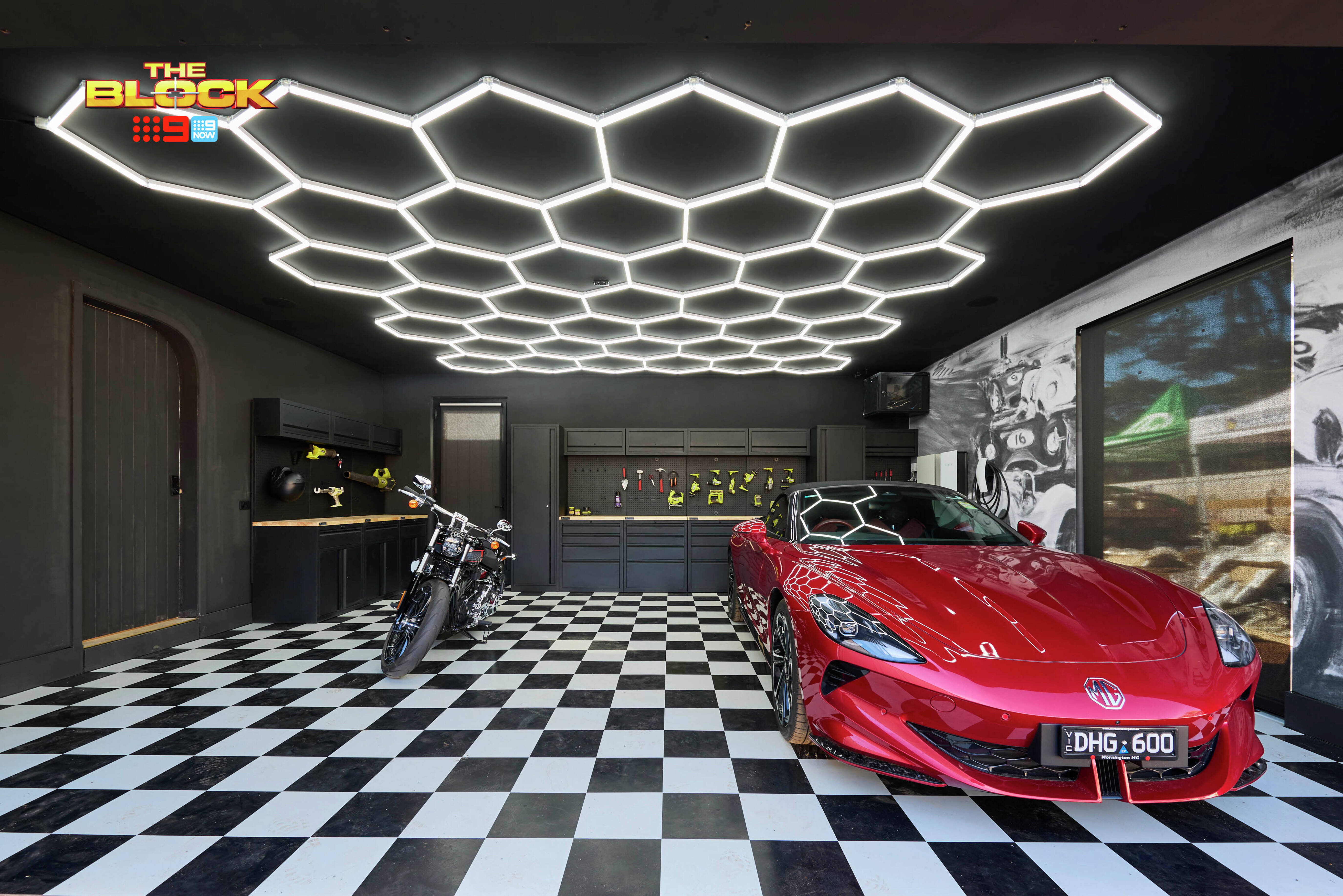 Stylish garage from The Block with checkered flooring, hexagonal LED ceiling lights, a red sports car, and a motorcycle.