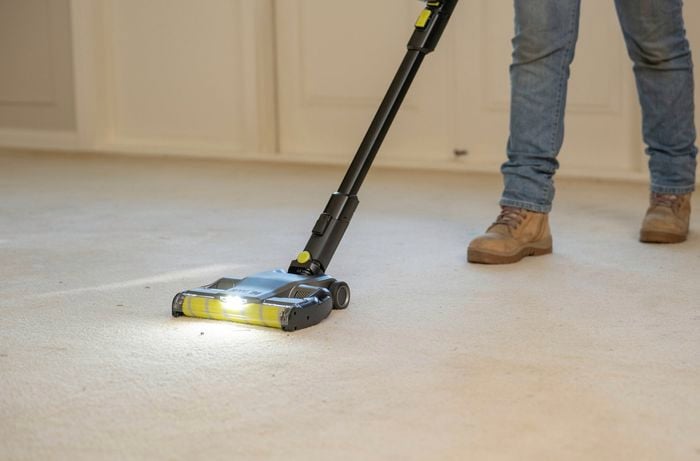 A person wearing work boots is thoroughly vacuum the carpet before starting the deep cleaning process