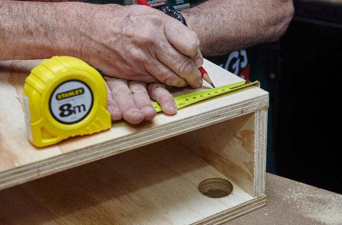 A person marking a measurement on a plywood box