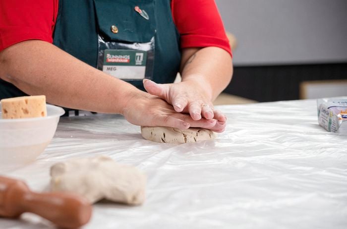 A person flattening a fist sized piece of clay.