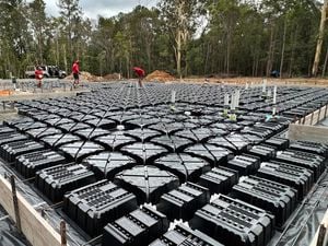 A construction site with a large grid of Biax pods inside timber framework, three tradespeople in red shirts walk across the setup, with bushland in the background