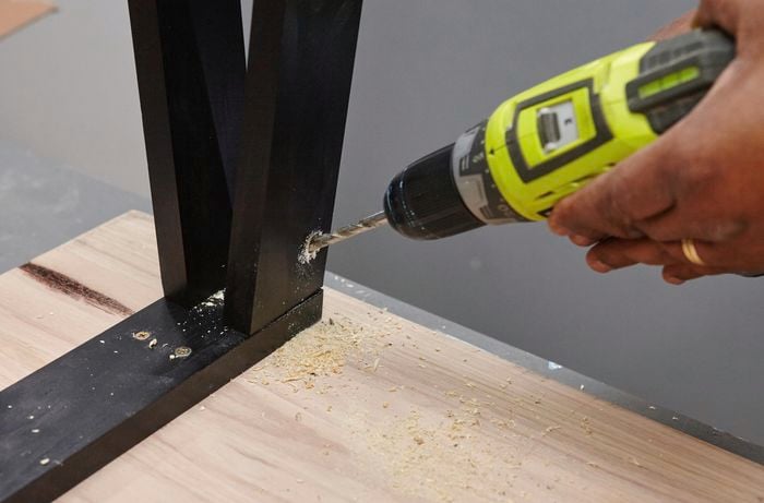 A person drilling into table legs on an inverted table