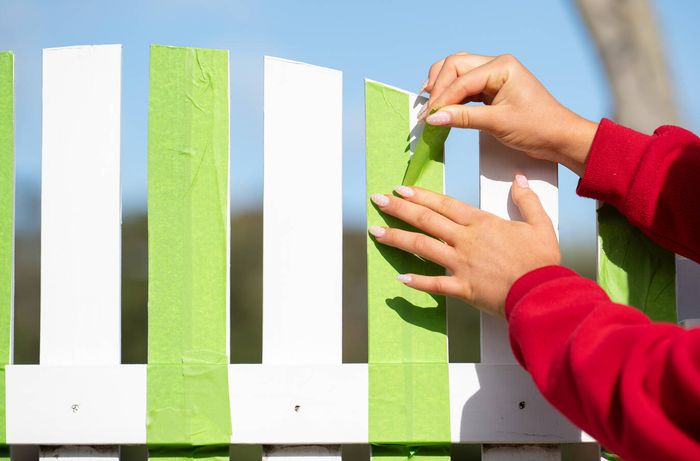Applying painter's tape to selected fence palings before painting stripes.