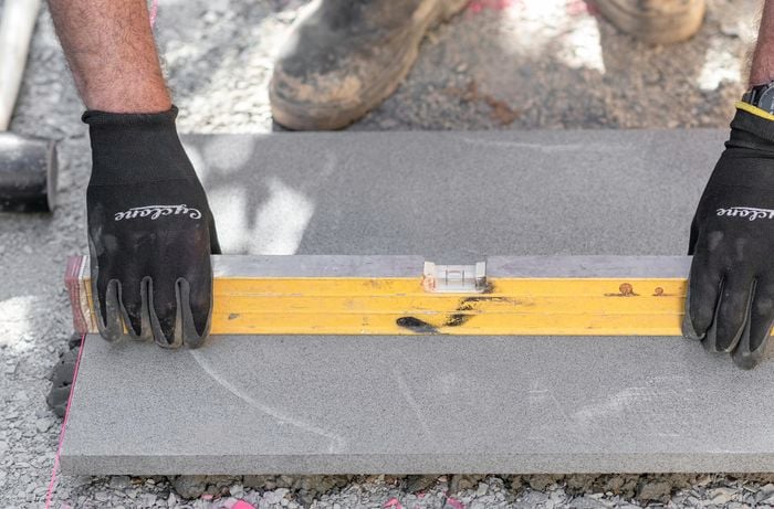 Person wearing protective gloves placing a spirit level across a paving stone.