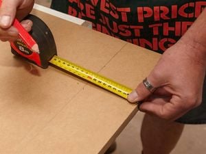Person marking measurements on a sheet of MDF
