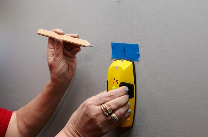 A person using a stud finder to mark the positions of studs onto masking tape on a wall
