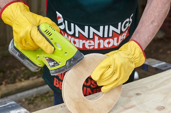 A person sanding a circle of plywood with an orbital sander