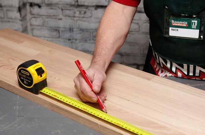 A length of timber being marked for cutting with a pencil and tape measure