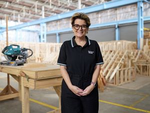 Bunnings Trade team member standing in a timber construction training workshop with woodworking equipment and timber framing in the background.