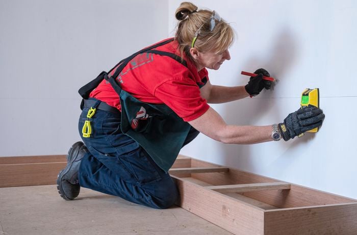 A person locating the studs in the wall using a stud finder.