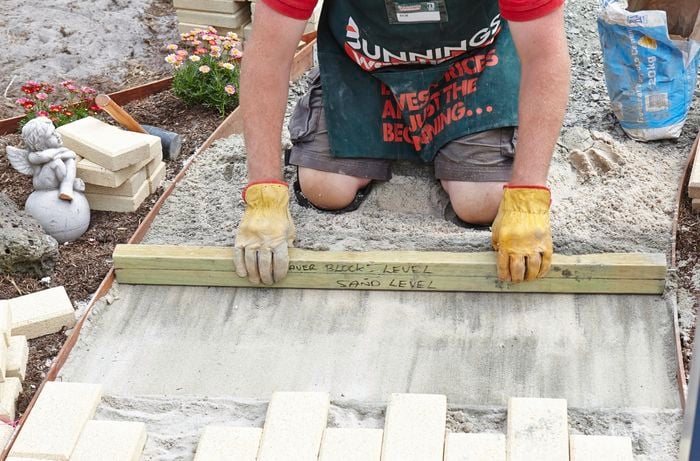 A person screeding the sand base of a pathway with a length of timber
