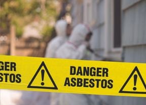 Yellow hazard tape in front of two hazmat workers with the words Danger Asbestos