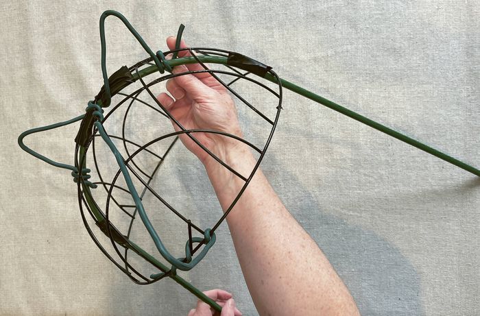 Hands shaping green twist ties around a wire hanging basket frame attached to a green garden U hoop.