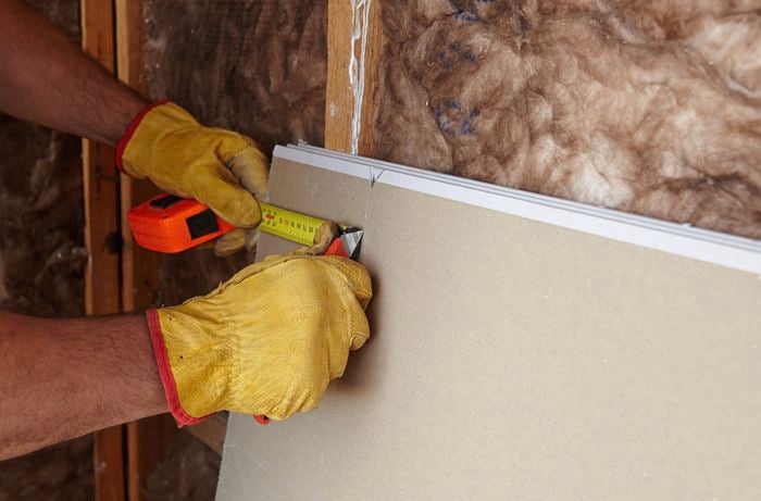 Plasterboard being measured and trimmed to size with a tape measure and boxcutter