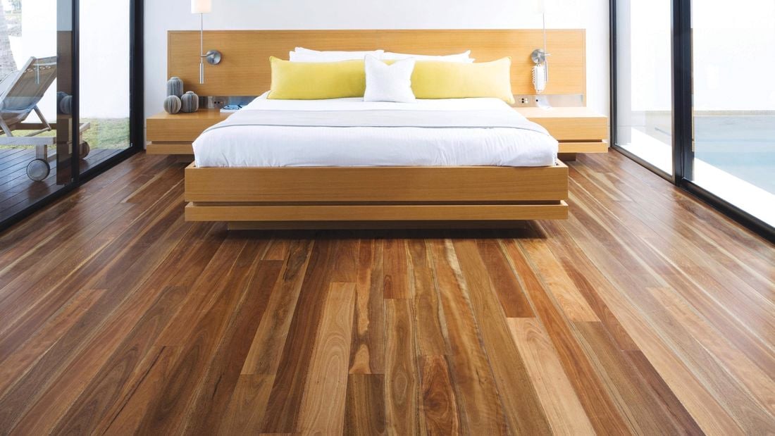 Modern bedroom featuring a timber bed frame and large windows, with polished timber flooring extending across the room.