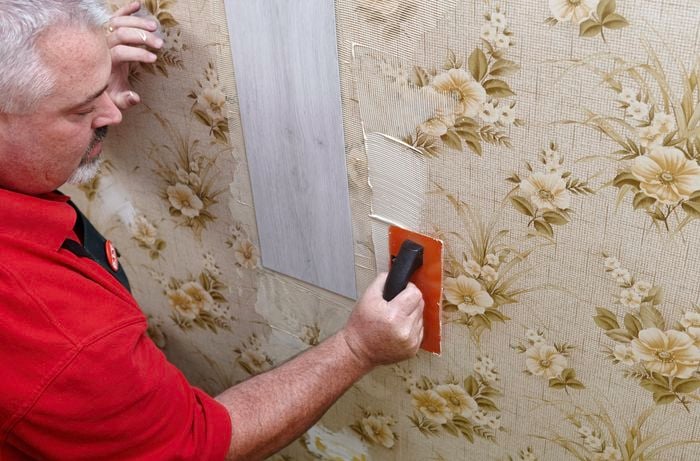 Plaster being applied to a wallpapered wall to stick on faux wooden panels