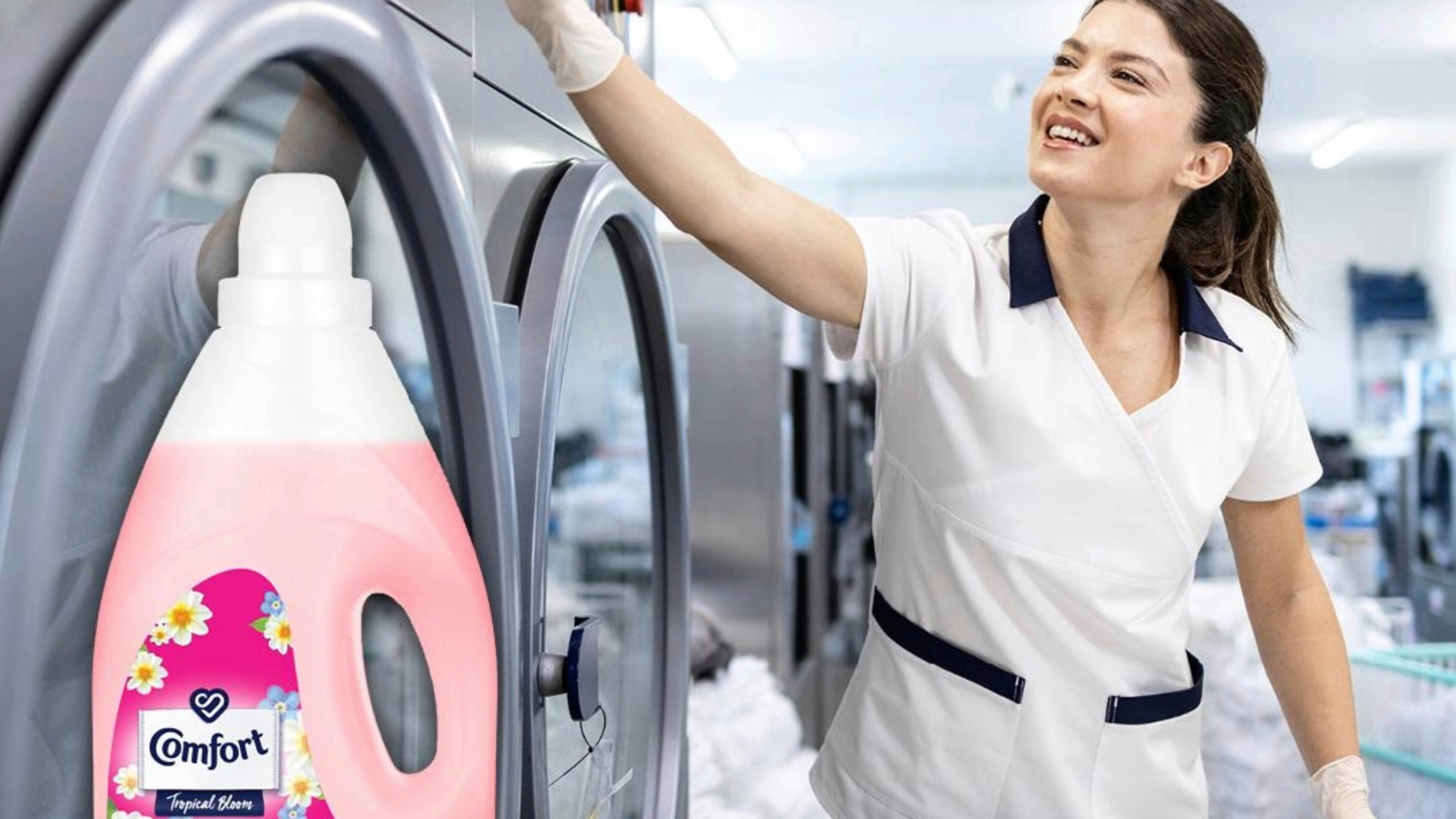 A woman in a white uniform next to a wall of washing machines with a bottle of Comfort fabric conditioner in the foreground