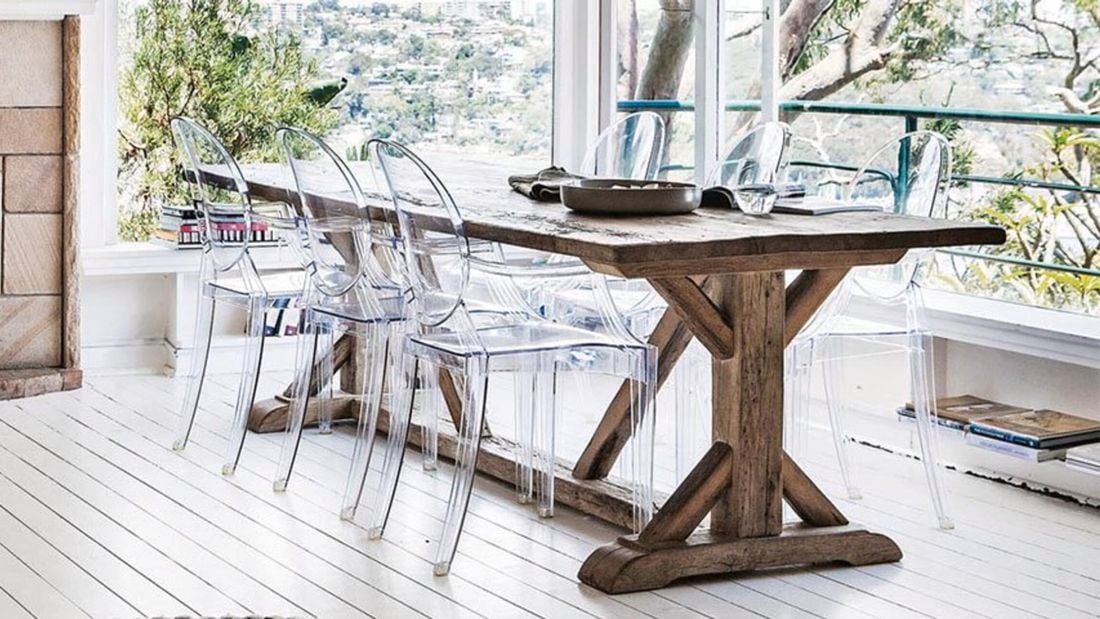 A rustic outdoor dining table paired with clear plastic chairs on an outdoor deck