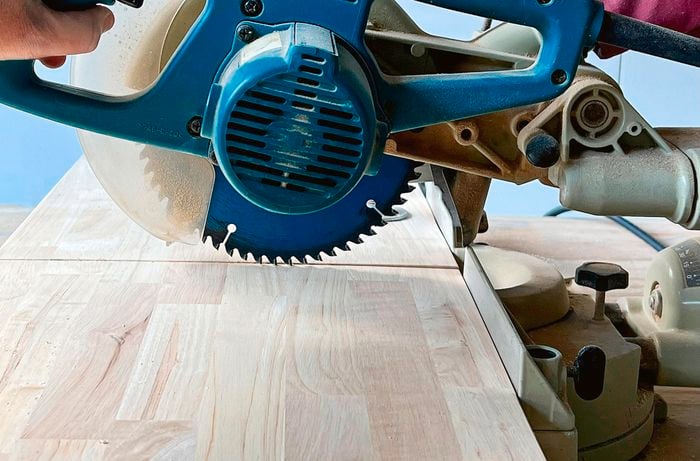 Pair of hands using a mitre saw to cut a panel of timber