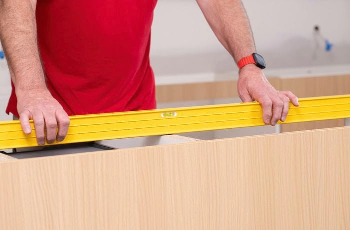 A person is using a spirit level along the top of the cabinets to check for flatness. 