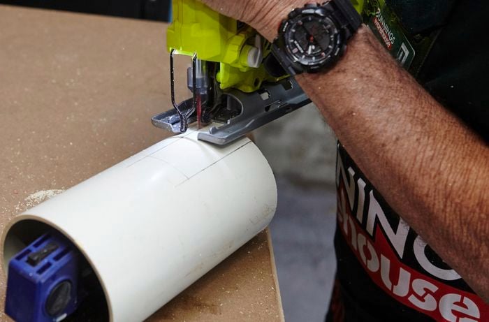 A person cutting a slot in a length of PVC pipe using a jigsaw
