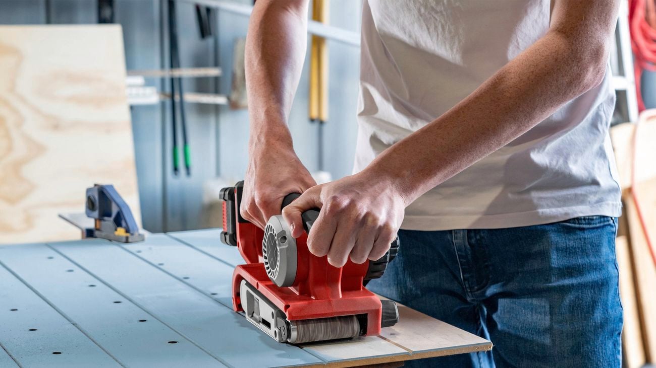 Person using a belt sander on panelling.