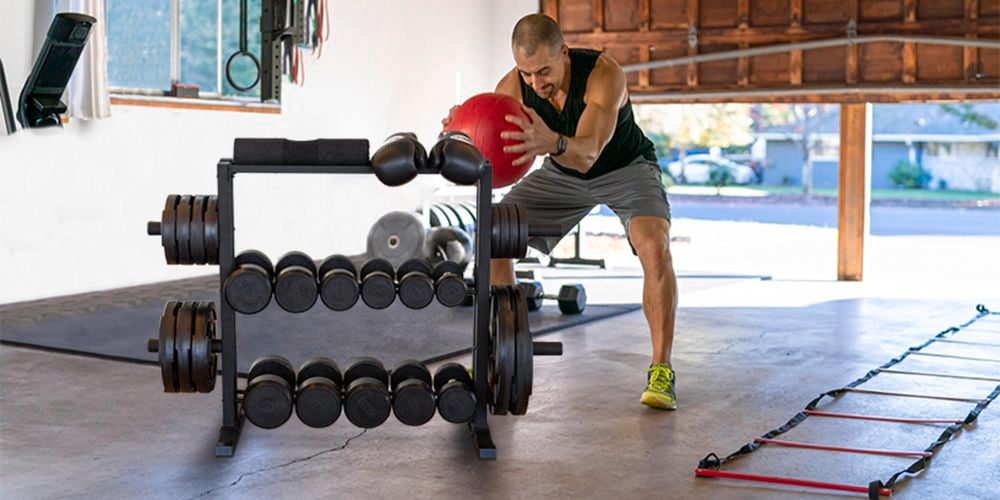 A man training with a gym ball in a home gym where dumbbells stored in a rack with 4 shelves.