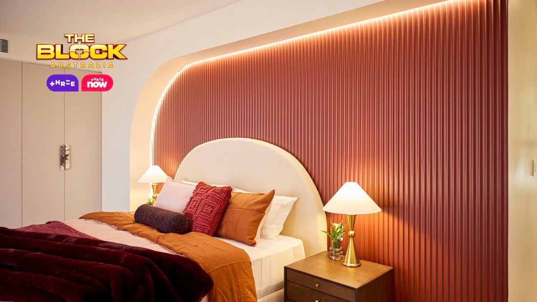 Bedroom with patterned wallpaper, pink bedding, and bedside lamps.
